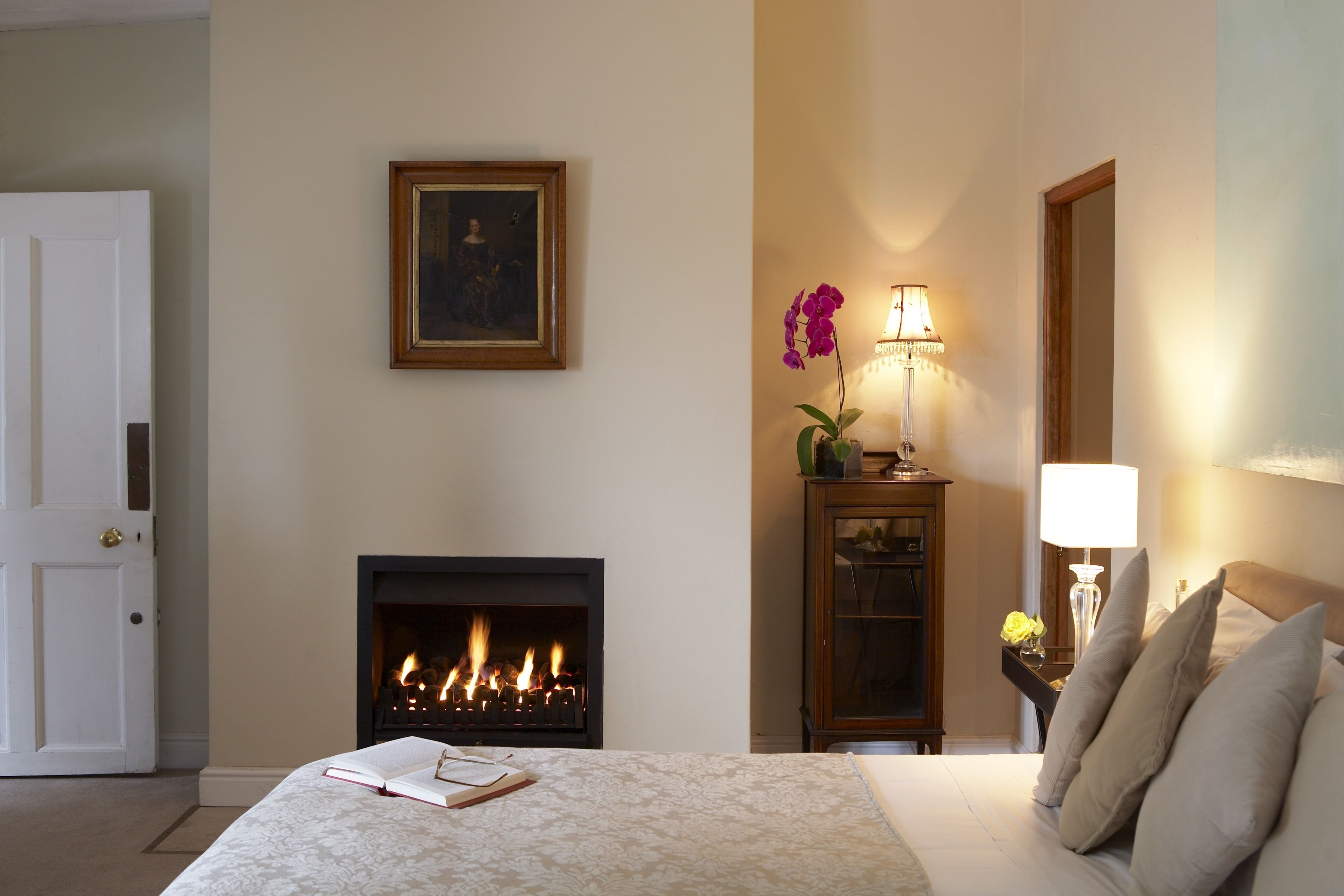 Een hotelkamer met een bed, een open haard, een nachtkastje met een lamp en een deur.