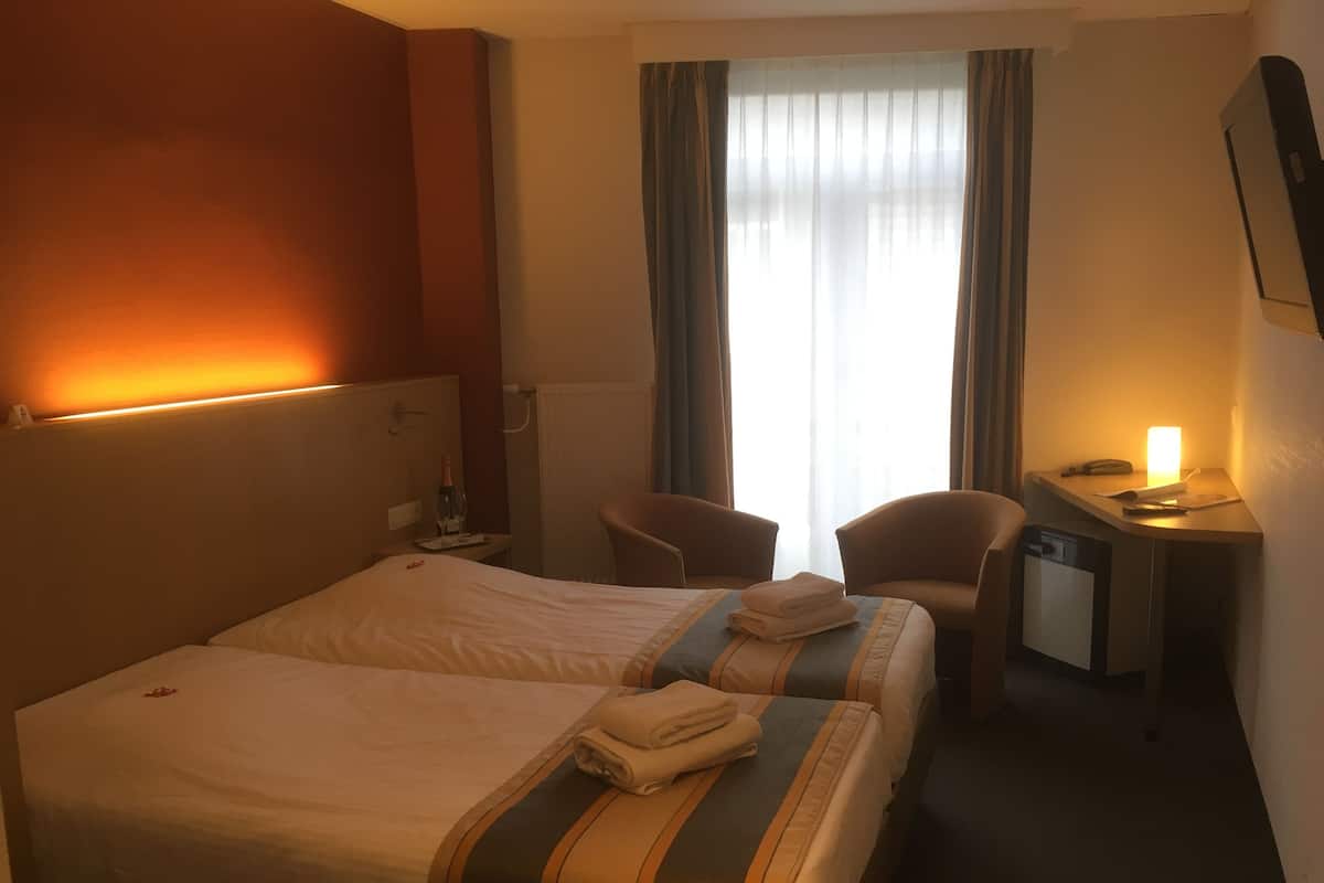 Ein Hotelzimmer mit zwei Betten, einem Schreibtisch, einem Stuhl und einem kleinen Fernseher.