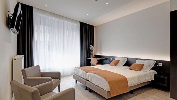 Una moderna camera d'albergo con un ampio letto, una scrivania, una sedia e un televisore fissato alla parete.