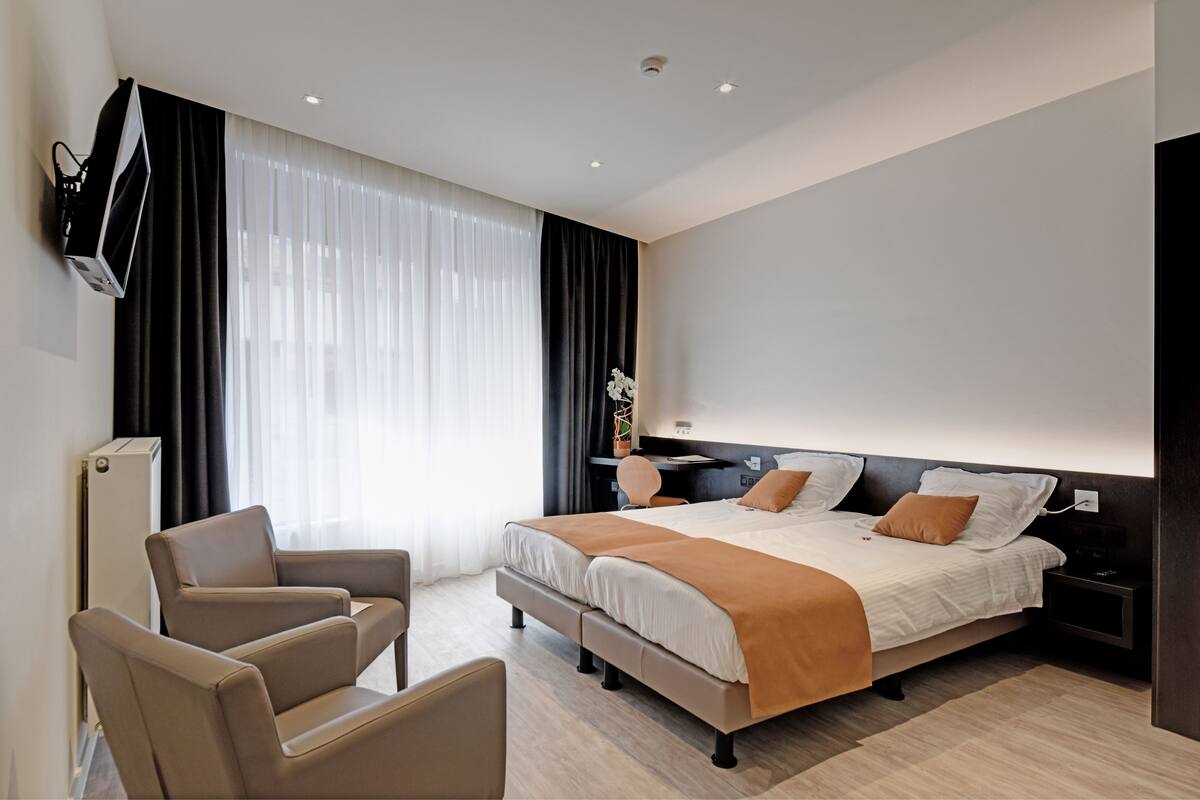 Ein modernes Hotelzimmer mit einem großen Bett, einem Schreibtisch, einem Sessel und einem an der Wand befestigten Fernseher.