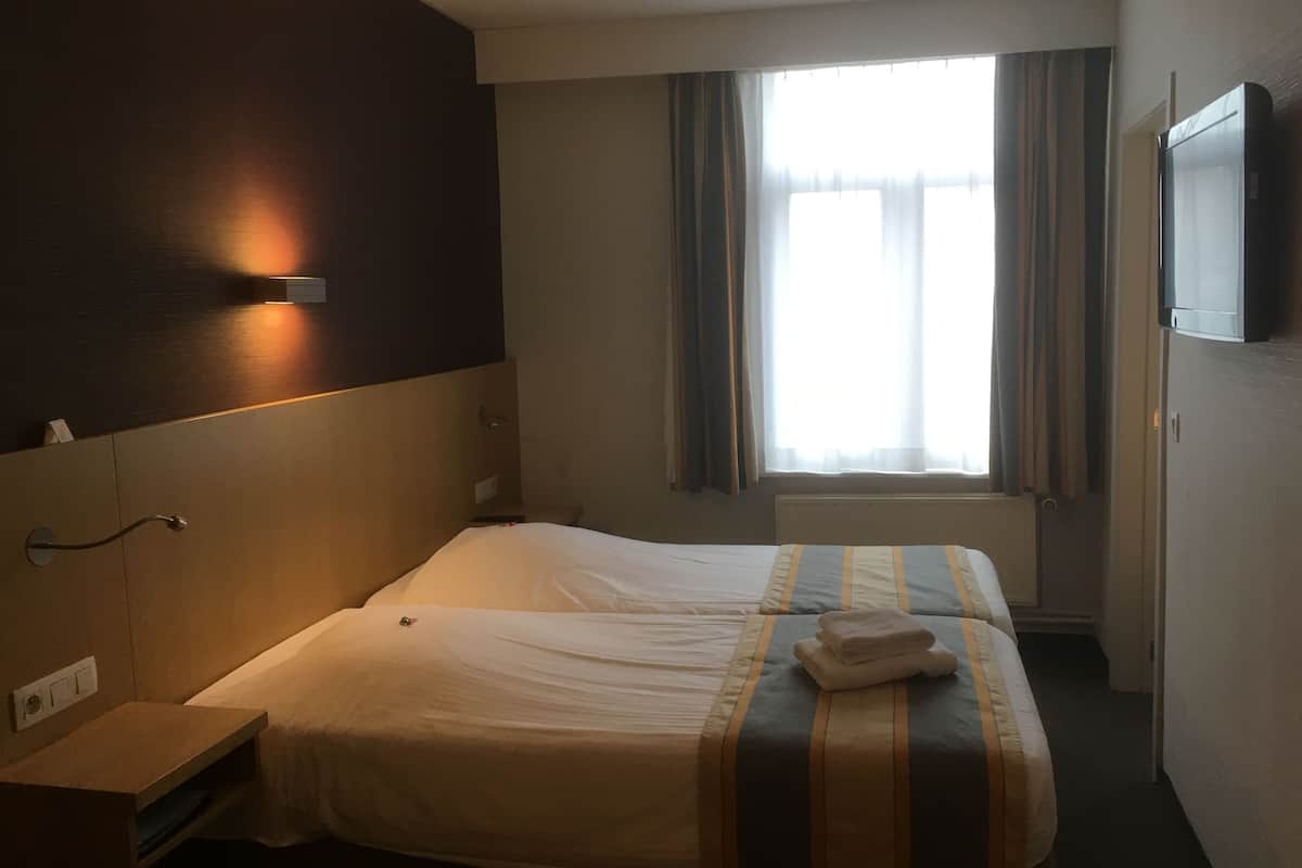 Ein Hotelzimmer mit Bett, Nachttisch, Fernseher und einem Fenster mit Vorhängen.