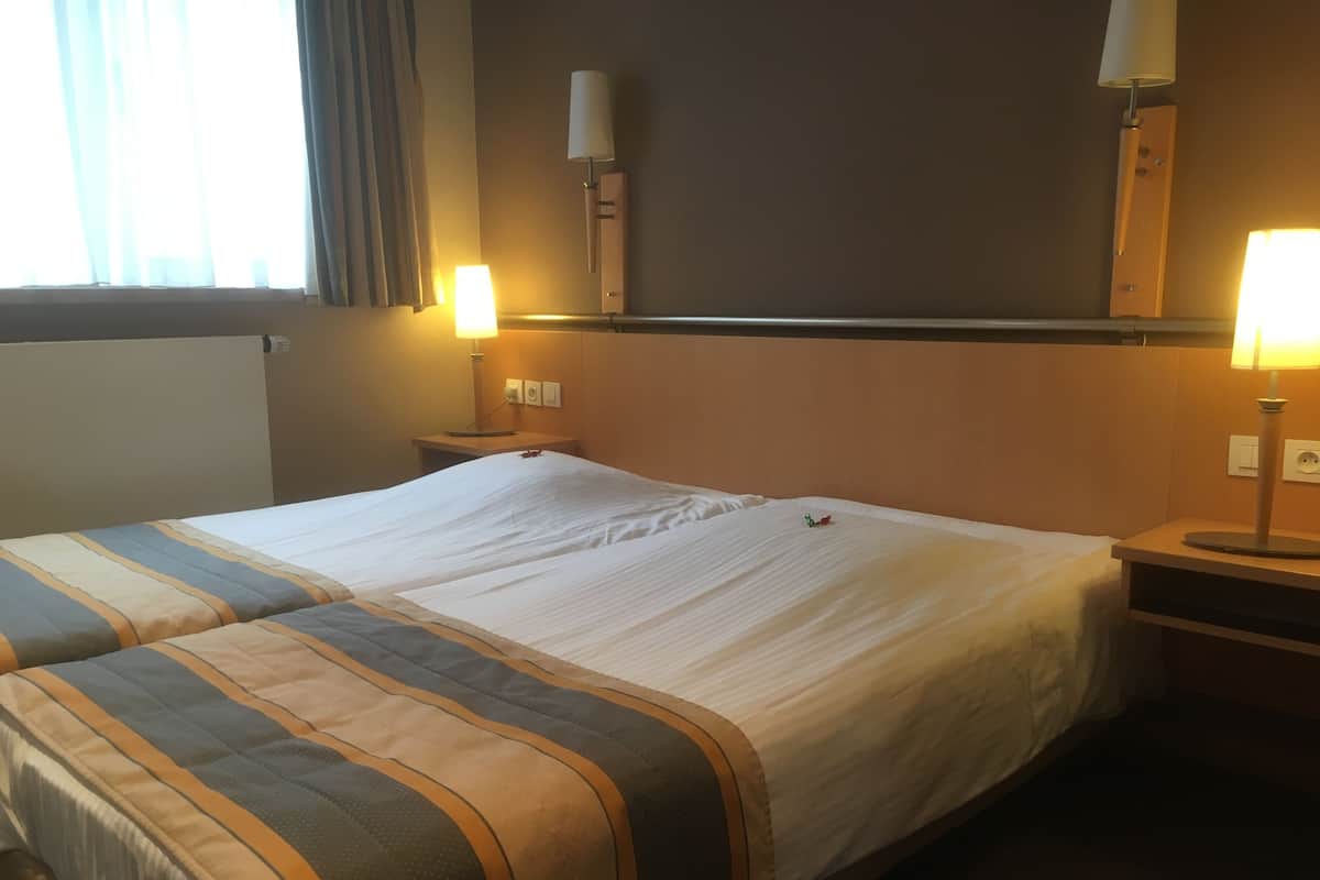 Ein Hotelzimmer mit zwei Betten, jeweils mit gestreifter Bettdecke, Nachttischlampen und einem Nachttisch.