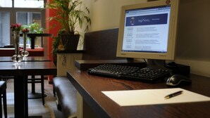 Una reception hotel con un computer, tastiera, mouse e una penna su un blocco note. C'è una pianta in vaso e un vaso con fiori sulla scrivania.