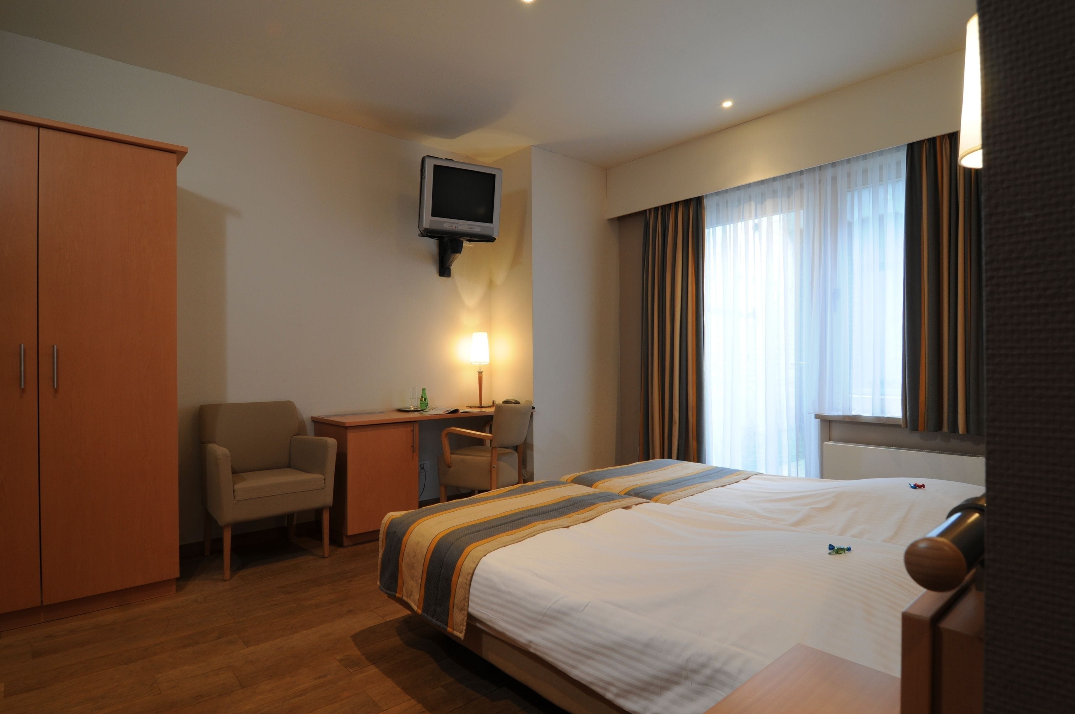 A hotel room with a bed, a desk, a chair, a television, and a wardrobe.