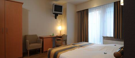 A hotel room with a bed, a desk, a chair, a television, and a wardrobe.