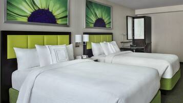 Habitación de hotel con dos camas, un cabecero tapizado en verde, ropa de cama blanca, una mesita de noche con lámpara y un espejo grande en la pared.