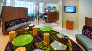 Un hall d’hôtel moderne avec un canapé, des poufs verts, une table basse et un téléviseur fixé au mur.