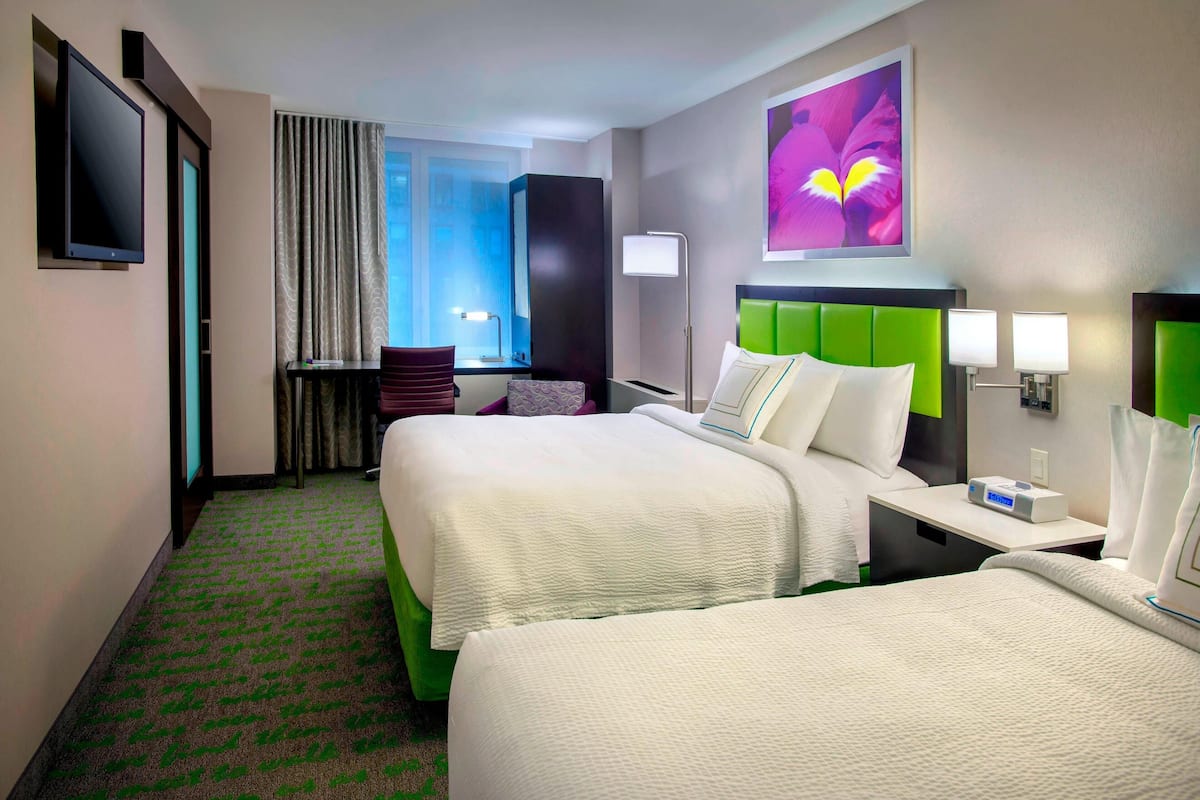 A hotel room with two beds, a flat-screen TV, a desk with a lamp, and a large window with curtains.