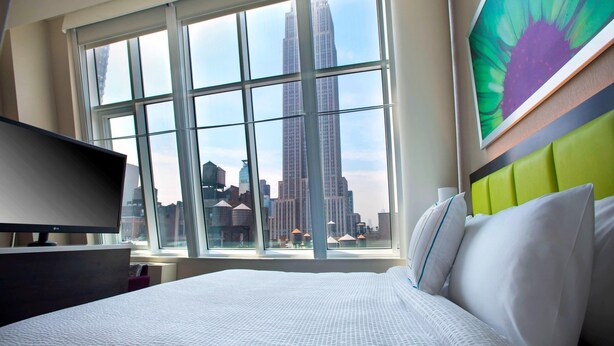 Une chambre d’hôtel avec une grande fenêtre, un lit, une télévision et une vue sur la ville.
