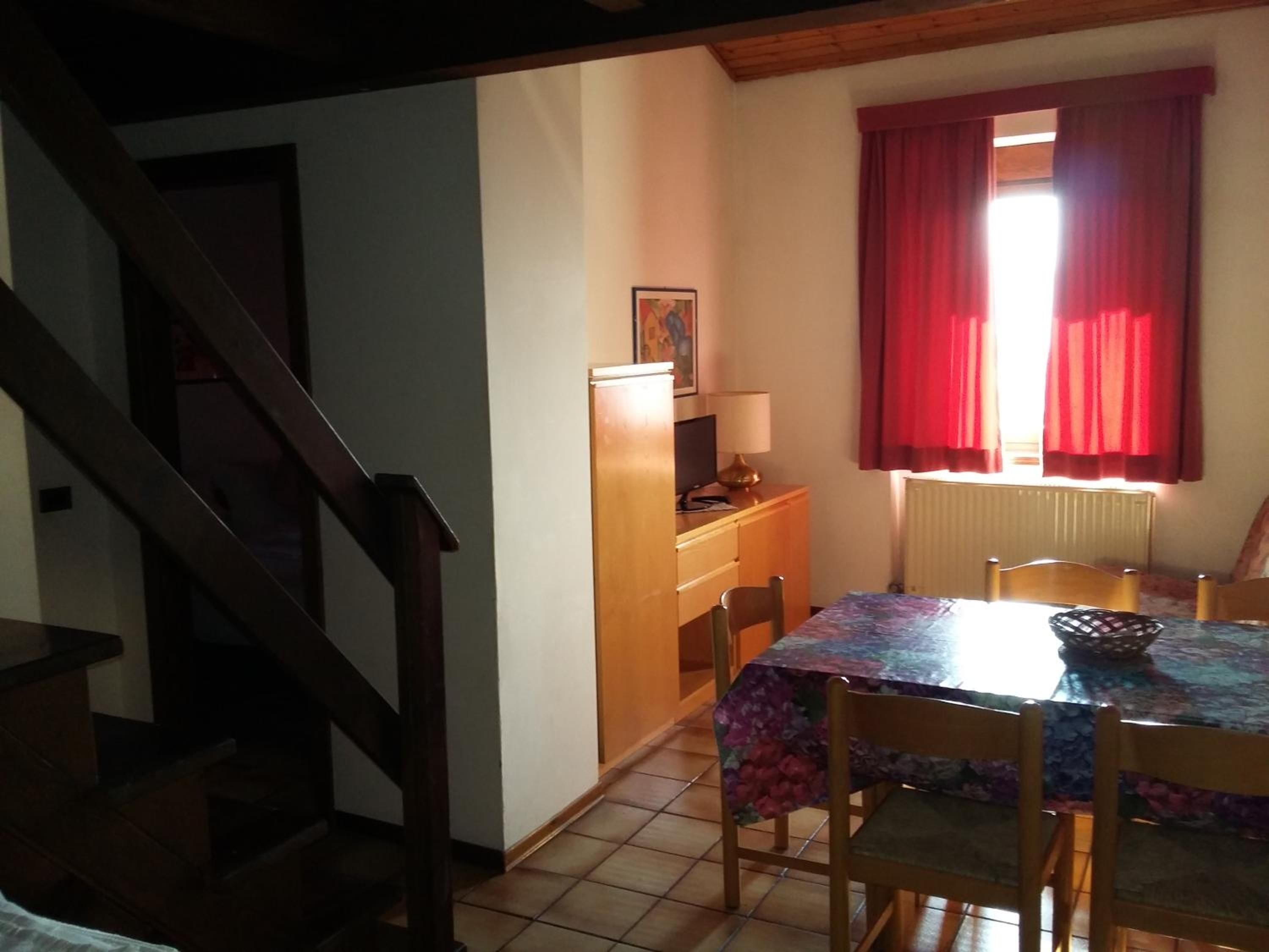 A dining area with a table, chairs, a lamp, and a window with curtains.