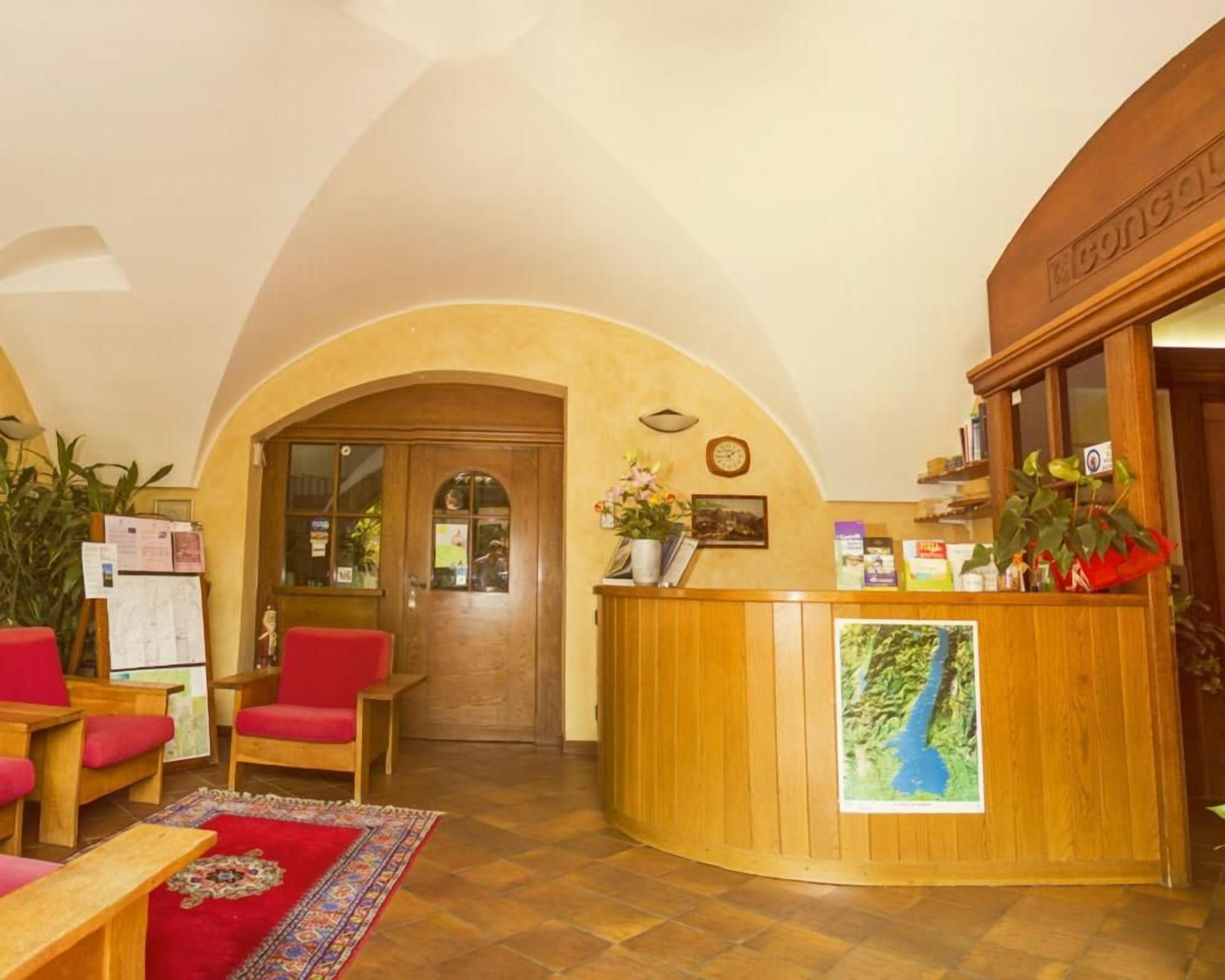 A reception area with a wooden reception desk, red chairs, a red carpet, and a clock on the wall.