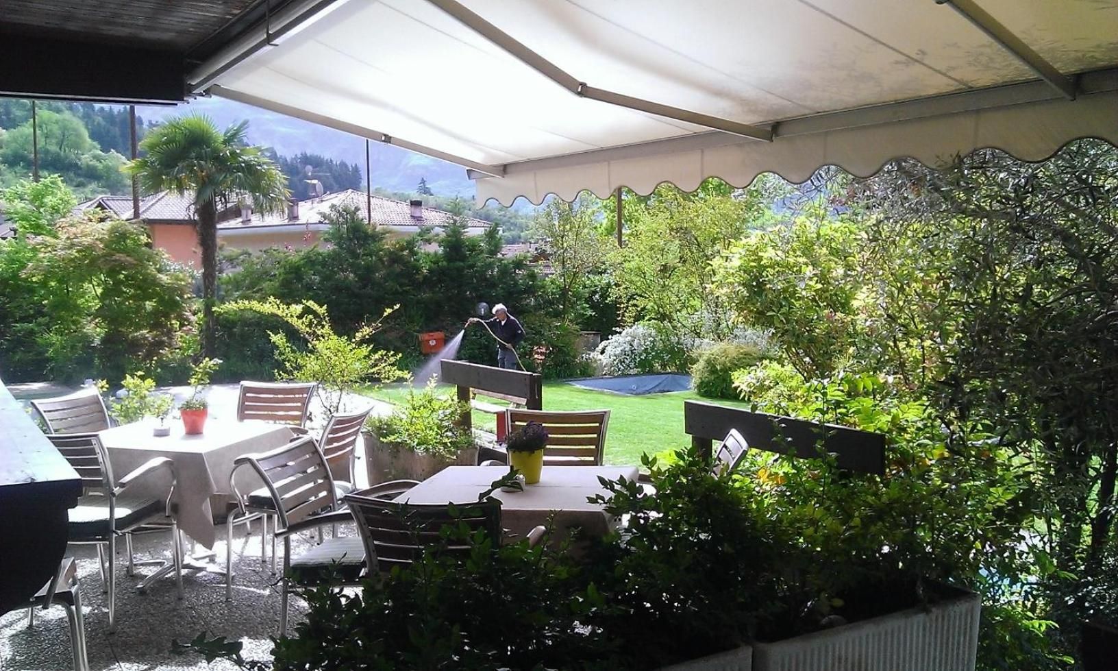 Eine Außenbereich-Terrasse mit Tisch und Stühlen, umgeben von üppiger Bepflanzung und Blick auf eine Wohngegend.