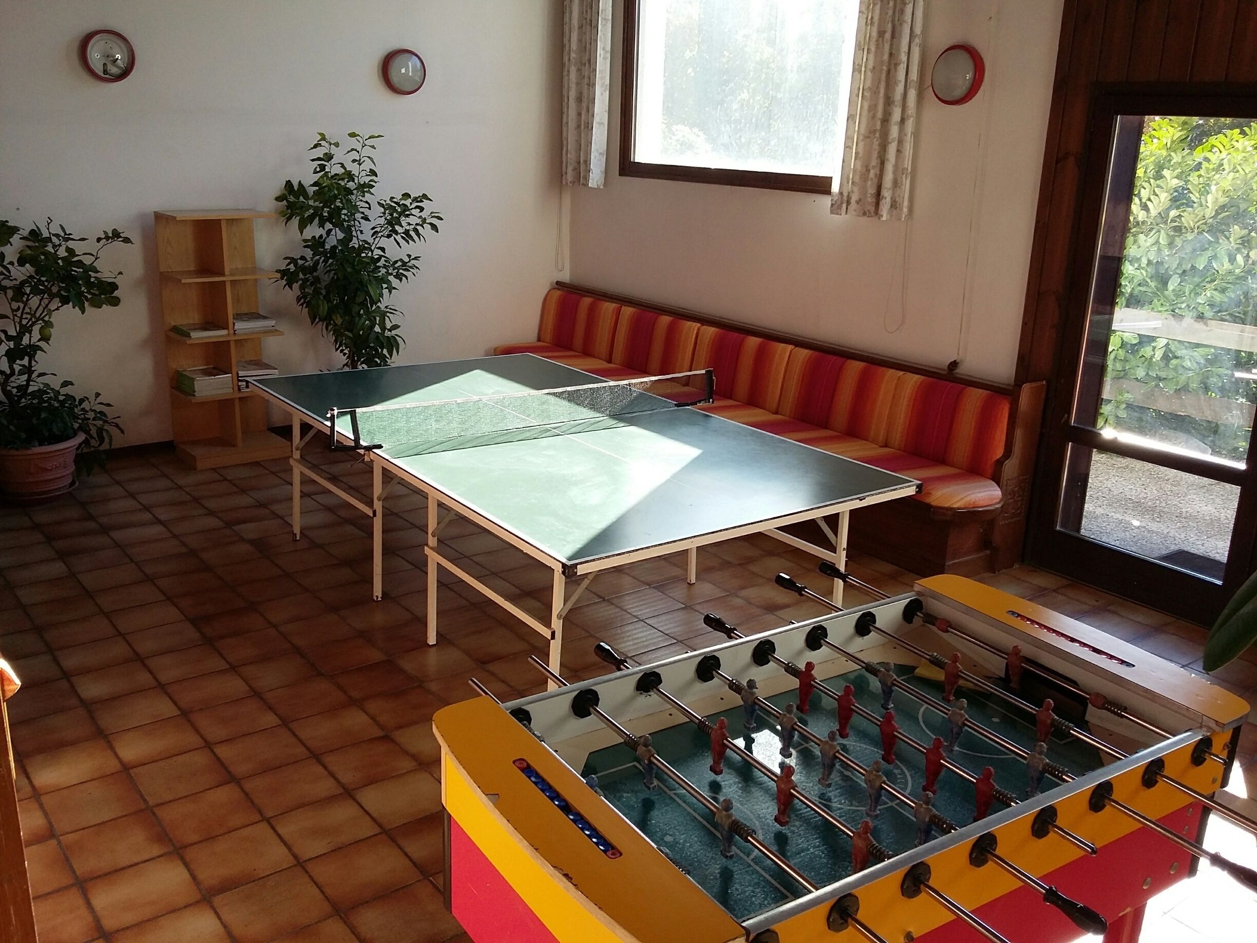 Una habitación con mesa de ping pong, sofá, estantería y mesa de fútbolín.