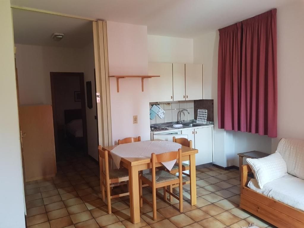 Ein kompakter Wohnbereich mit Esstisch und Stühlen, einer Küchenzeile, einer Couch und einem Fenster mit Vorhängen.