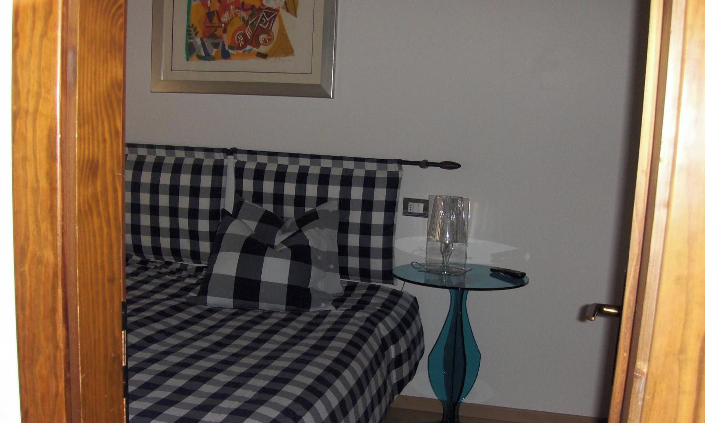 A room with a checkered sofa, a glass table with a remote, and a painting on the wall.