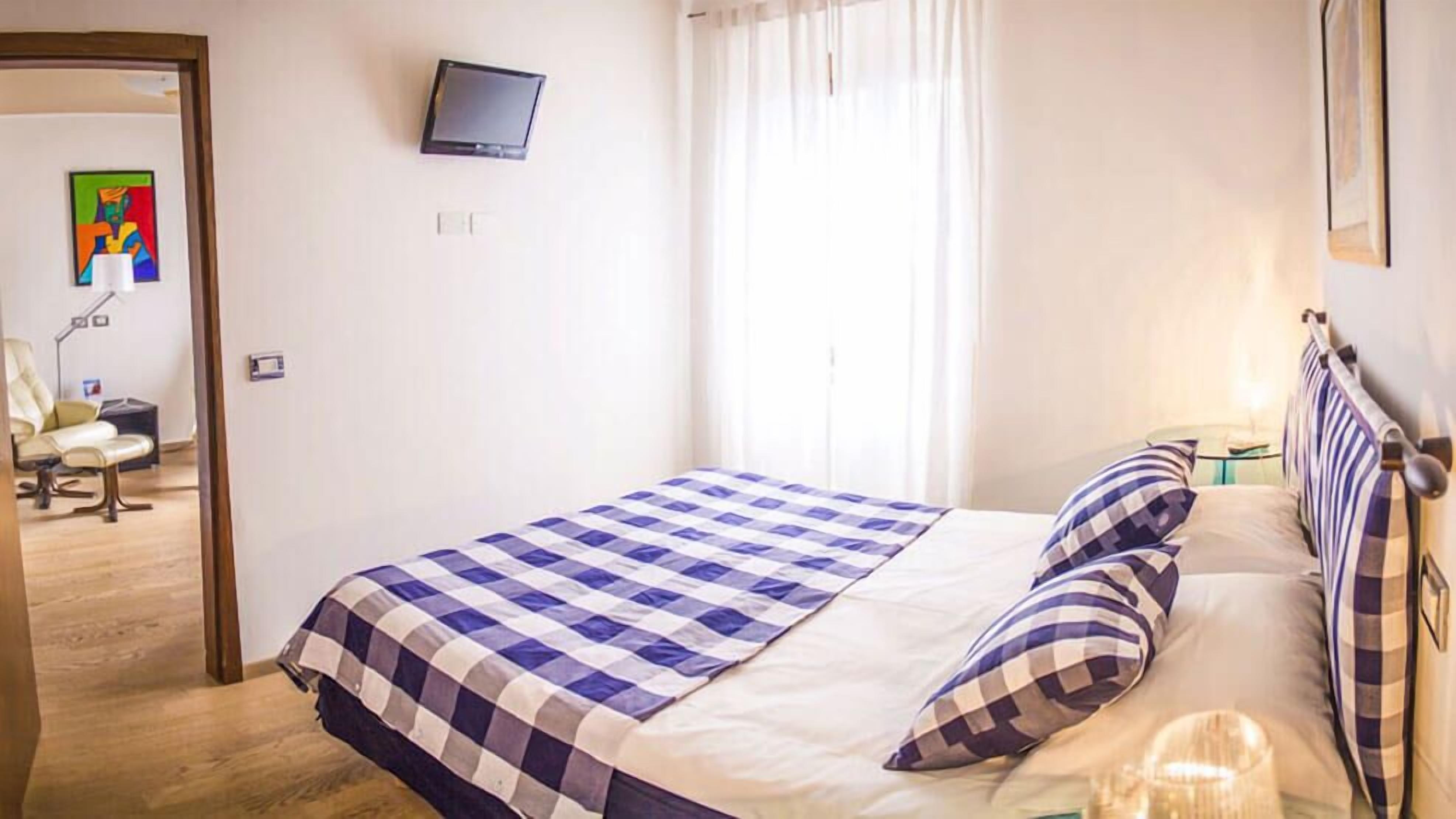 Ein Schlafzimmer mit kariertem Bettbezug, einem an der Wand befestigten Fernseher und einem Sessel in der Ecke.