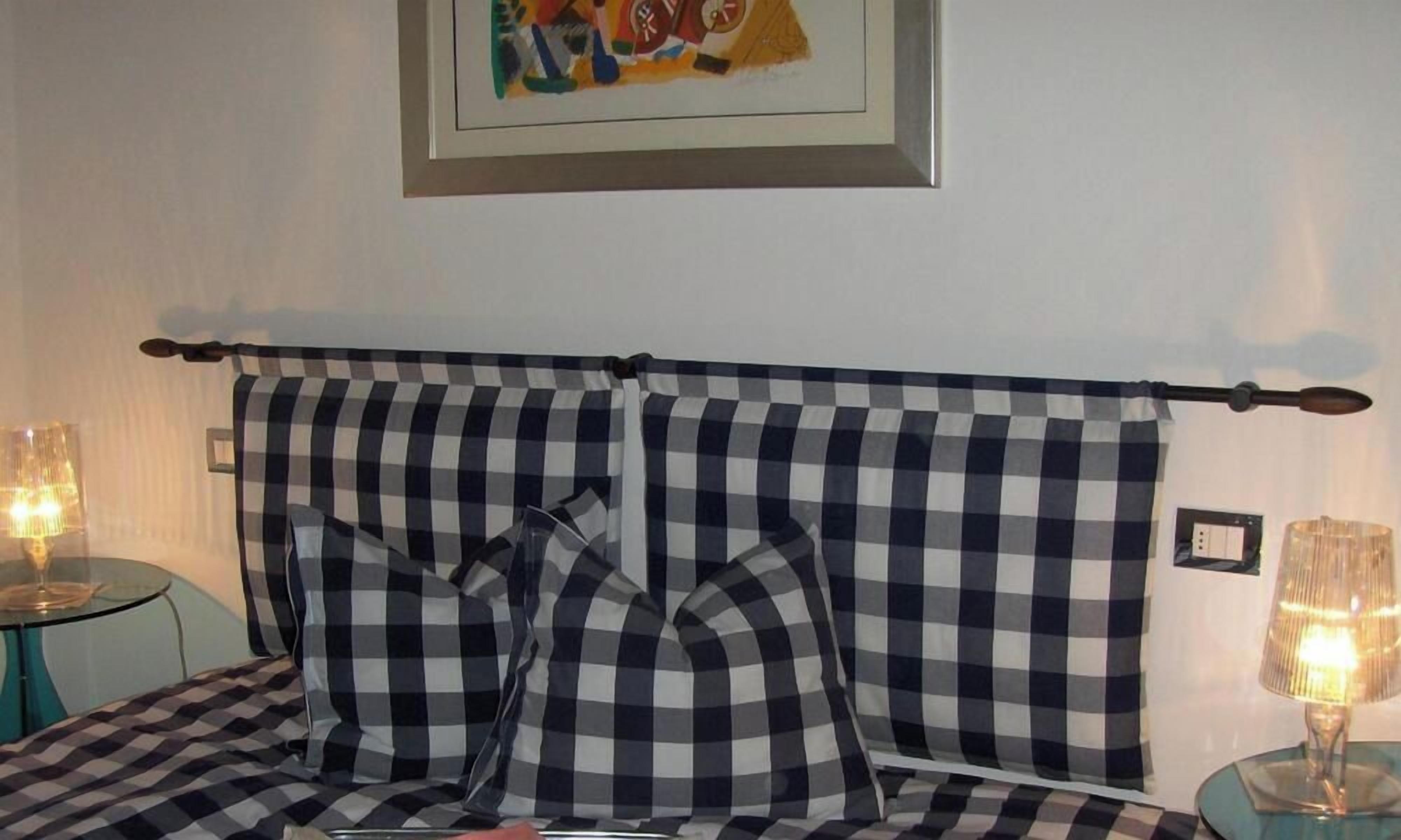Een bed met een geruit hoofdeinde, twee bedlampjes en een ingelijst schilderij aan de muur.