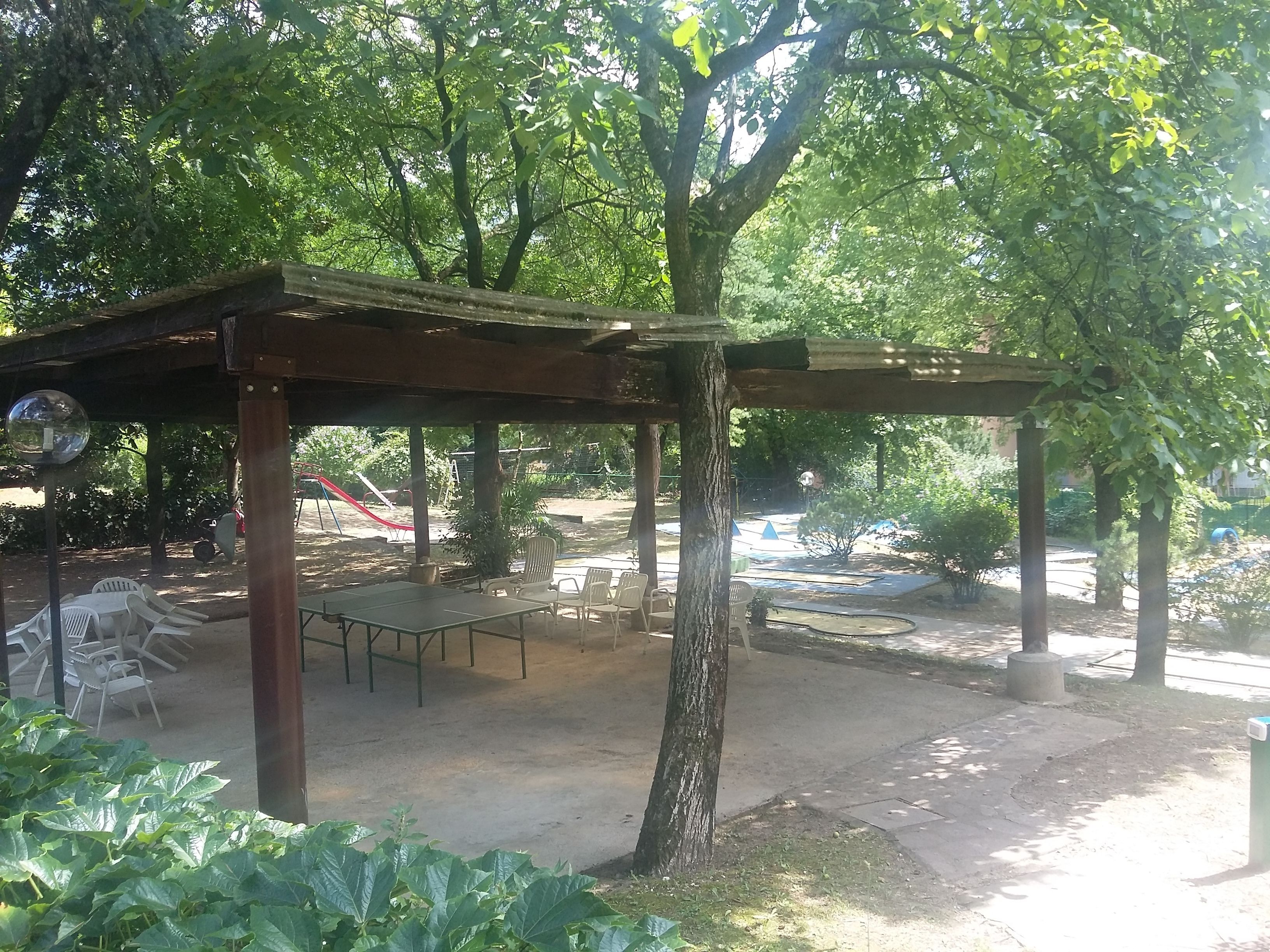 Un espace extérieur abrité, aménagé avec des tables et des chaises, et entouré d’arbres et de verdure.