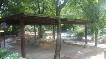 Un espace extérieur abrité, aménagé avec des tables et des chaises, et entouré d’arbres et de verdure.