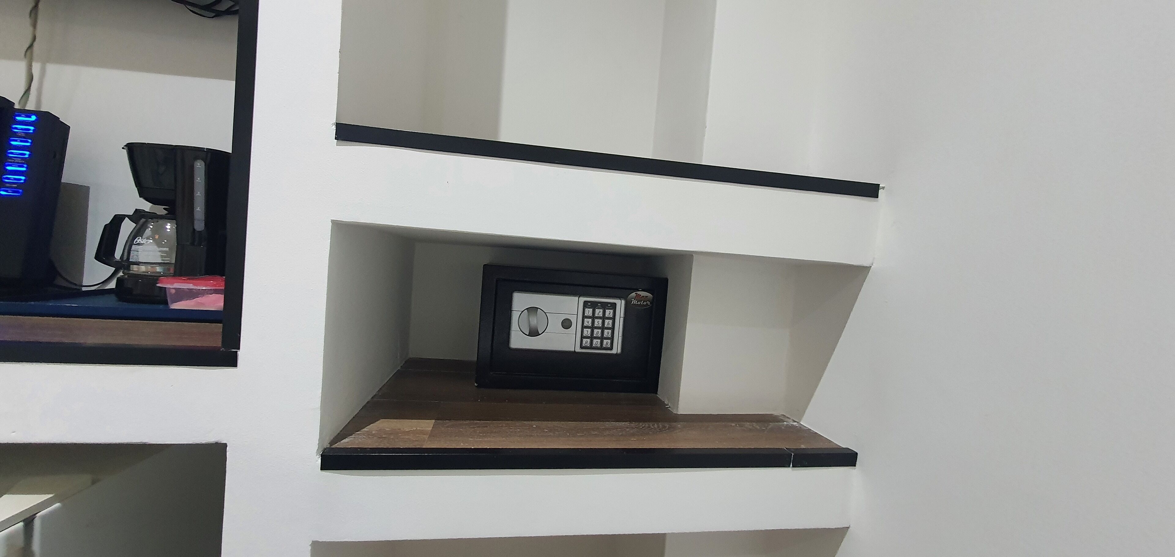 A secure safe on a shelf in a room with white walls and a black countertop.