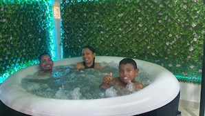 A hot tub with three people in it, surrounded by a green wall with flowers and a decorative lantern. - Posada Turística Colors Of The Sea (San Andrés)