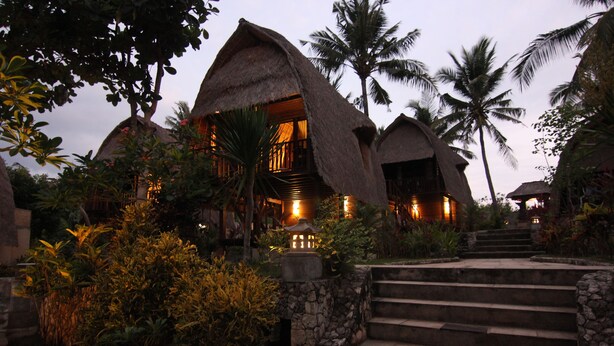Een resort met villa's met rieten daken, stenen trappen en tropische begroeiing.