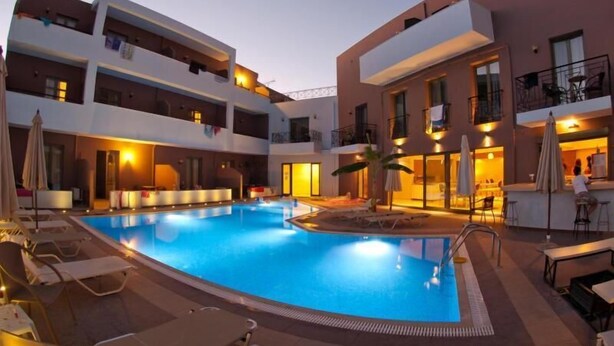 A swimming pool surrounded by lounge chairs and a bar area, with buildings in the background. - Hotel Stella Katrin (Rethymno)