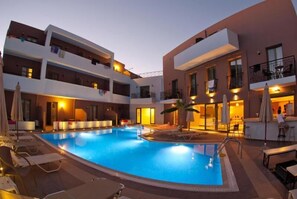 A swimming pool surrounded by lounge chairs and a bar area, with buildings in the background.