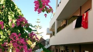 A modern building with balconies, a small garden with pink flowers, and a clear sky. - Hotel Stella Katrin (Rethymno)