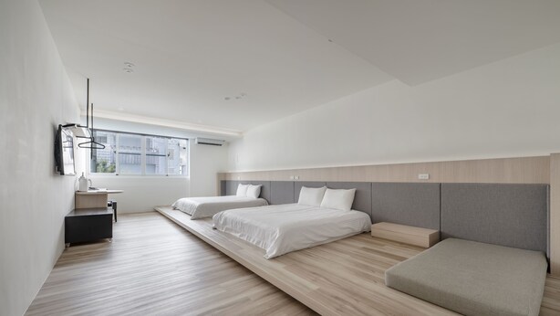 Quarto moderno com duas camas, uma secretária pequena e uma janela.