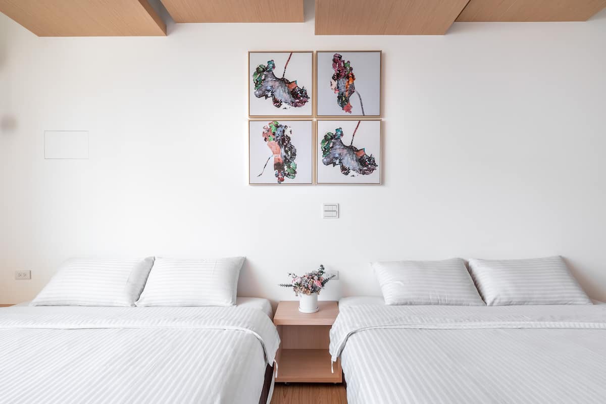 Ein Hotelzimmer mit zwei Betten, einem Nachttisch mit Blumenvase und vier gerahmten Kunstwerken an der Wand.