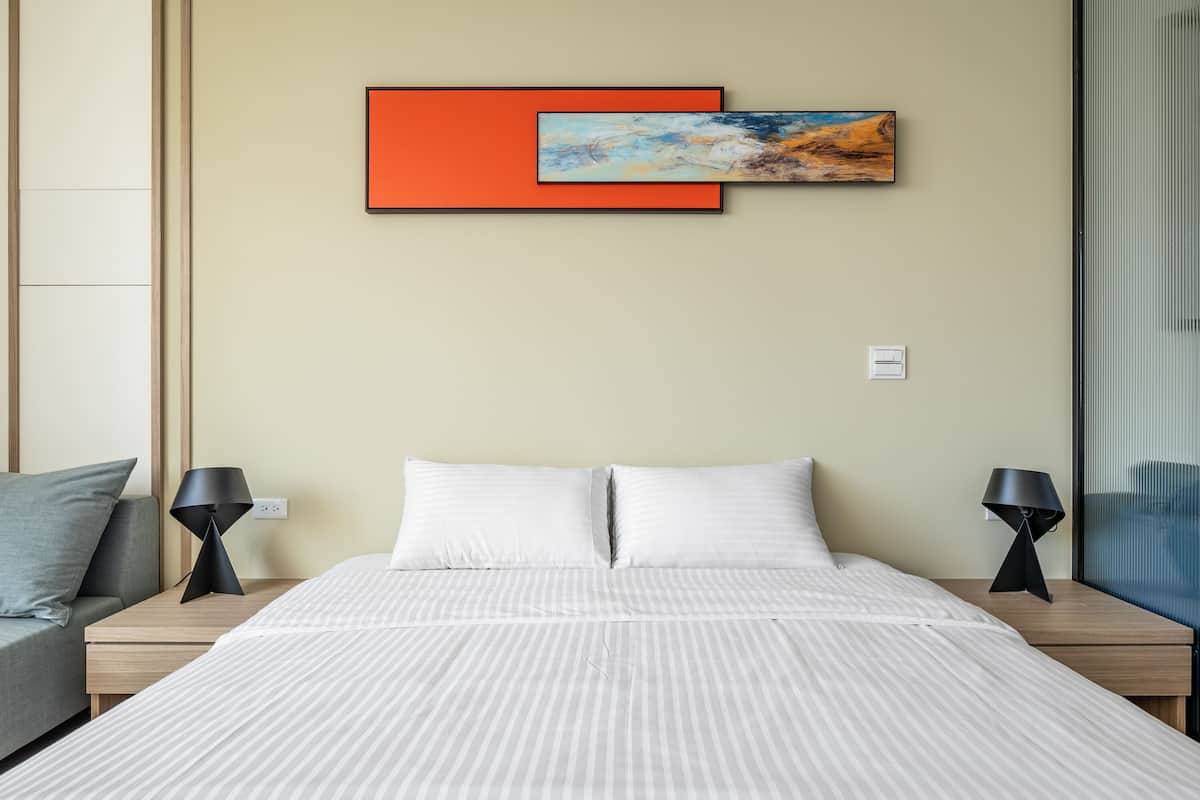 Ein ordentlich bezogenes Bett mit gestreifter Bettwäsche, zwei Nachttischlampen und ein an der Wand befestigtes abstraktes Gemälde.