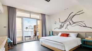 Quarto de hotel moderno com cama grande, vista para o exterior, área de refeições e uma obra de arte na parede.