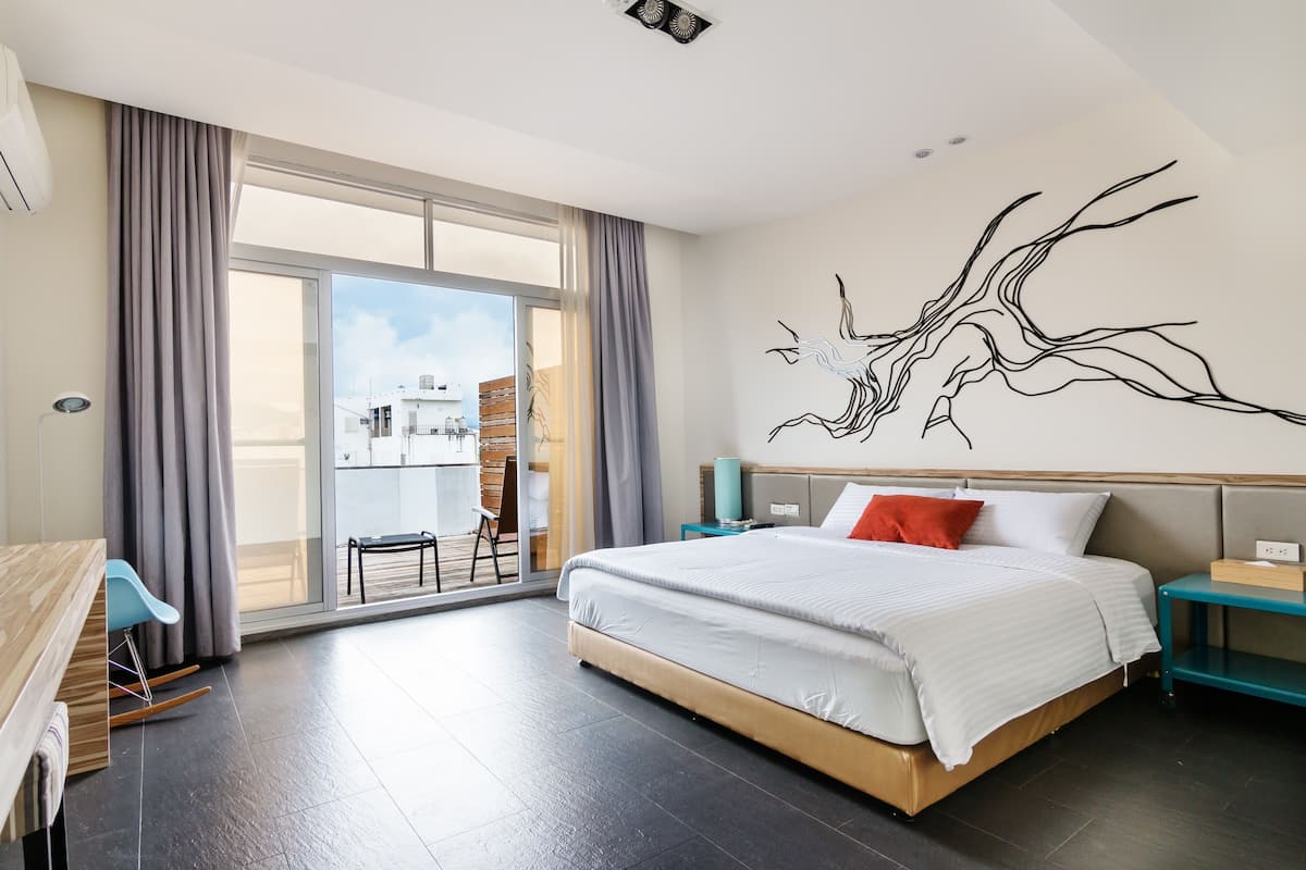 Ein modernes Hotelzimmer mit einem großen Bett, Blick ins Freie, einer Essecke und einem Wandbild.