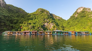A row of floating houses with a clear view of lush green mountains in the background. - Heritage Line Violet cruise – Ha Long Bay & Lan Ha Bay  (Tuan Chau)