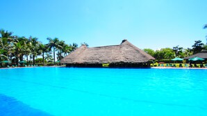 A clear blue pool with a thatched-roof structure in the center, surrounded by palm trees and lounge chairs. - Speke Resort & Conference Centre (Kampala)