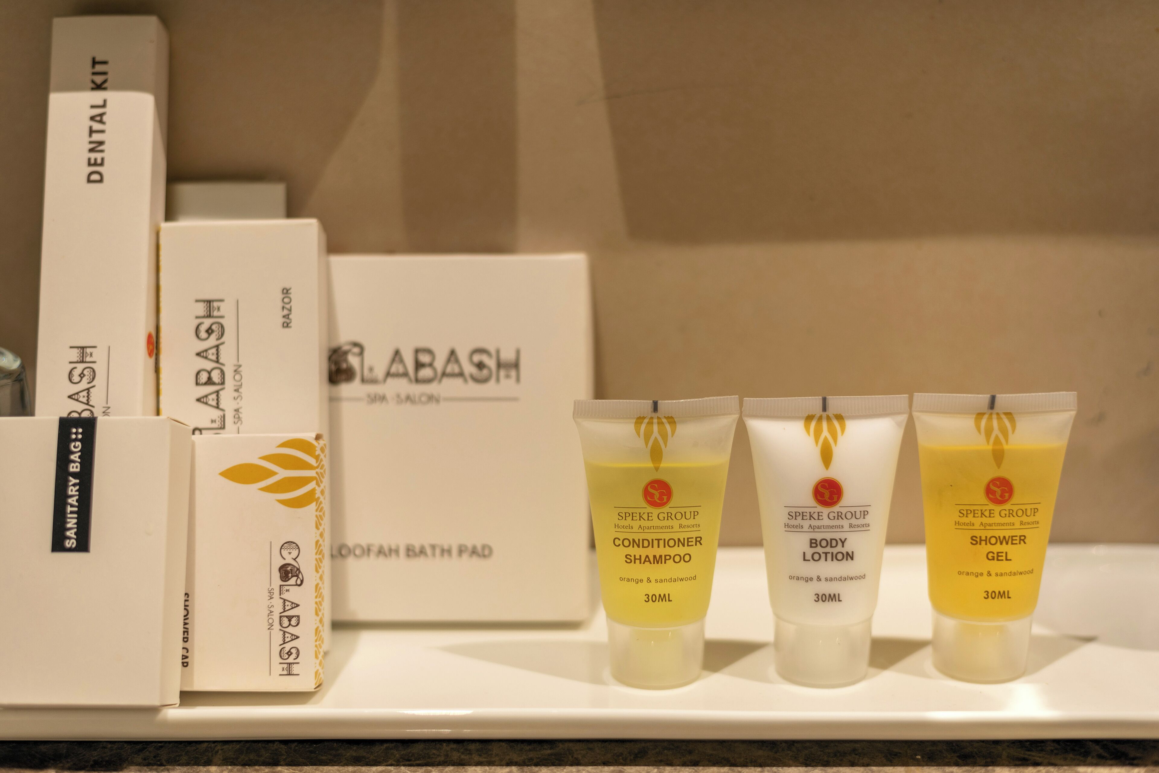 Un estante con diversos artículos de spa y baño, incluyendo un kit dental, una alfombra de baño con esponja, acondicionador, champú, loción corporal y gel de ducha.