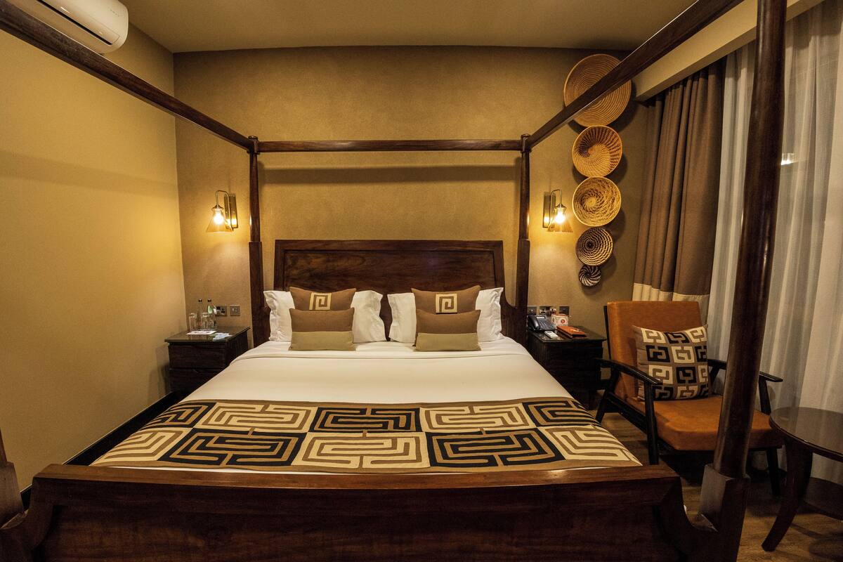 A four-poster bed with a geometric-patterned bedspread, a wooden headboard, and two bedside lamps.