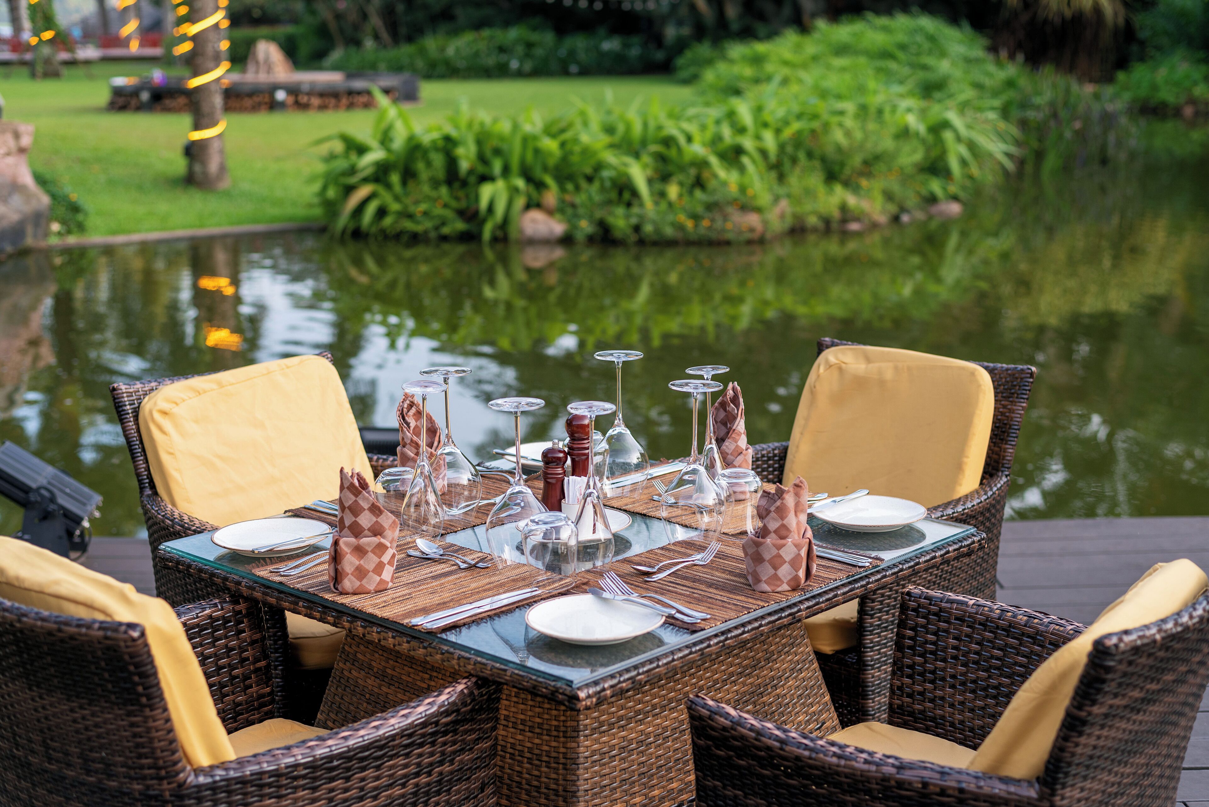 A dining table set with chairs, surrounded by a pond and greenery.