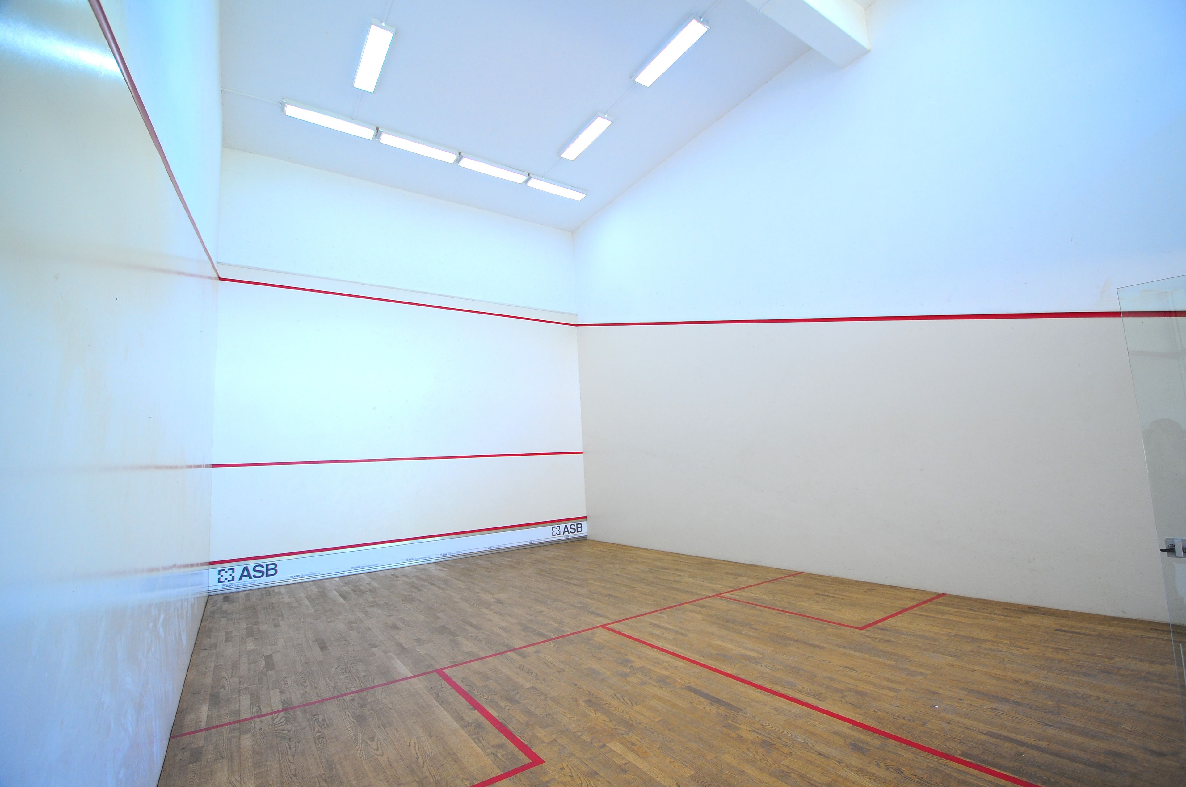 A squash court with white walls, red lines marking the playing area, and a wooden floor.