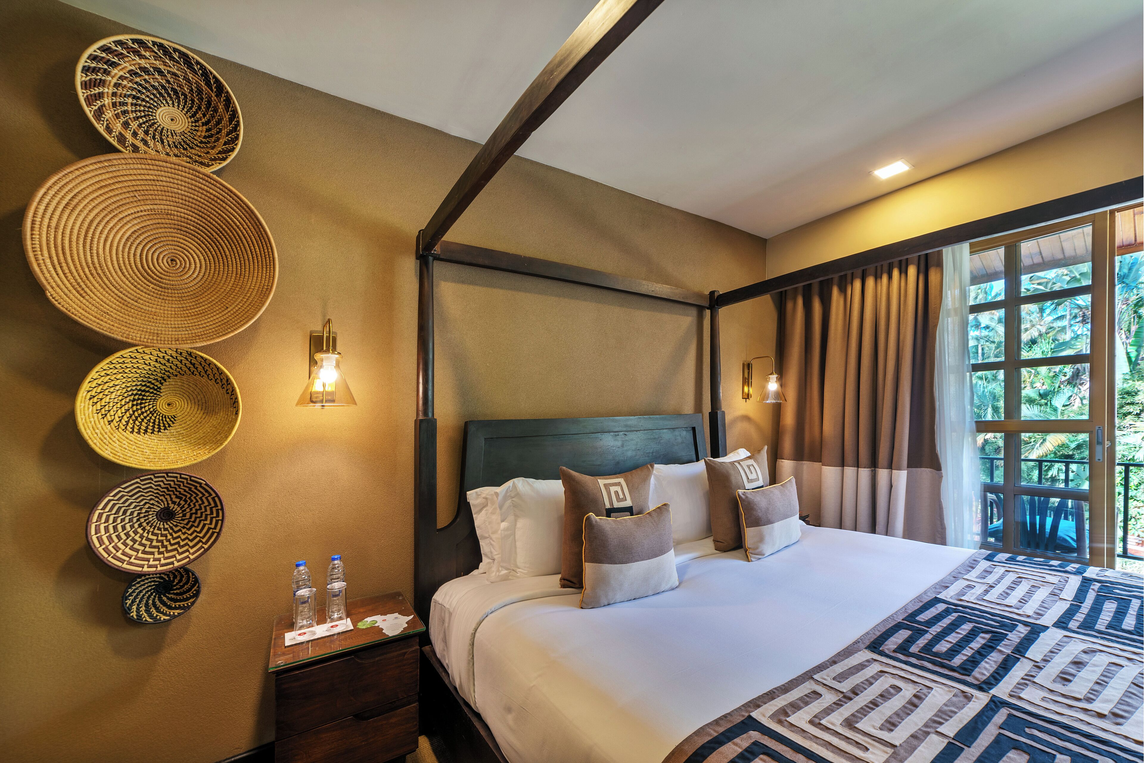 Ein Hotelzimmer mit einem großen Bett, einem Nachttisch, einer Wandlampe und einem mit Vorhängen versehenen Fenster.