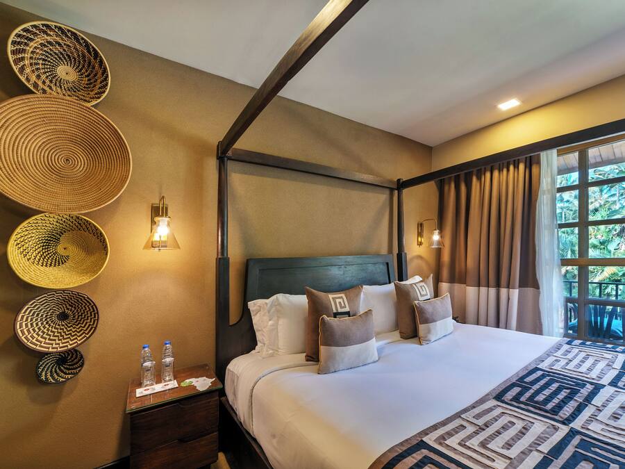 Ein Hotelzimmer mit einem großen Bett, einem Nachttisch, einer Wandlampe und einem mit Vorhängen versehenen Fenster.
