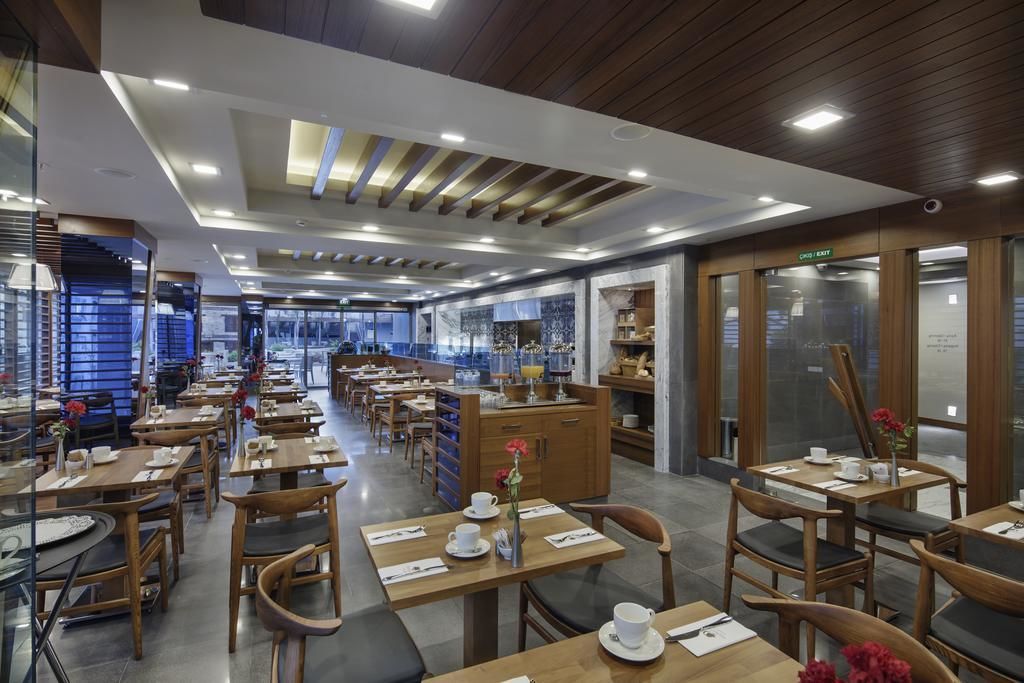 A modern dining area with wooden tables and chairs, a central counter with a display, and a view of the kitchen area.