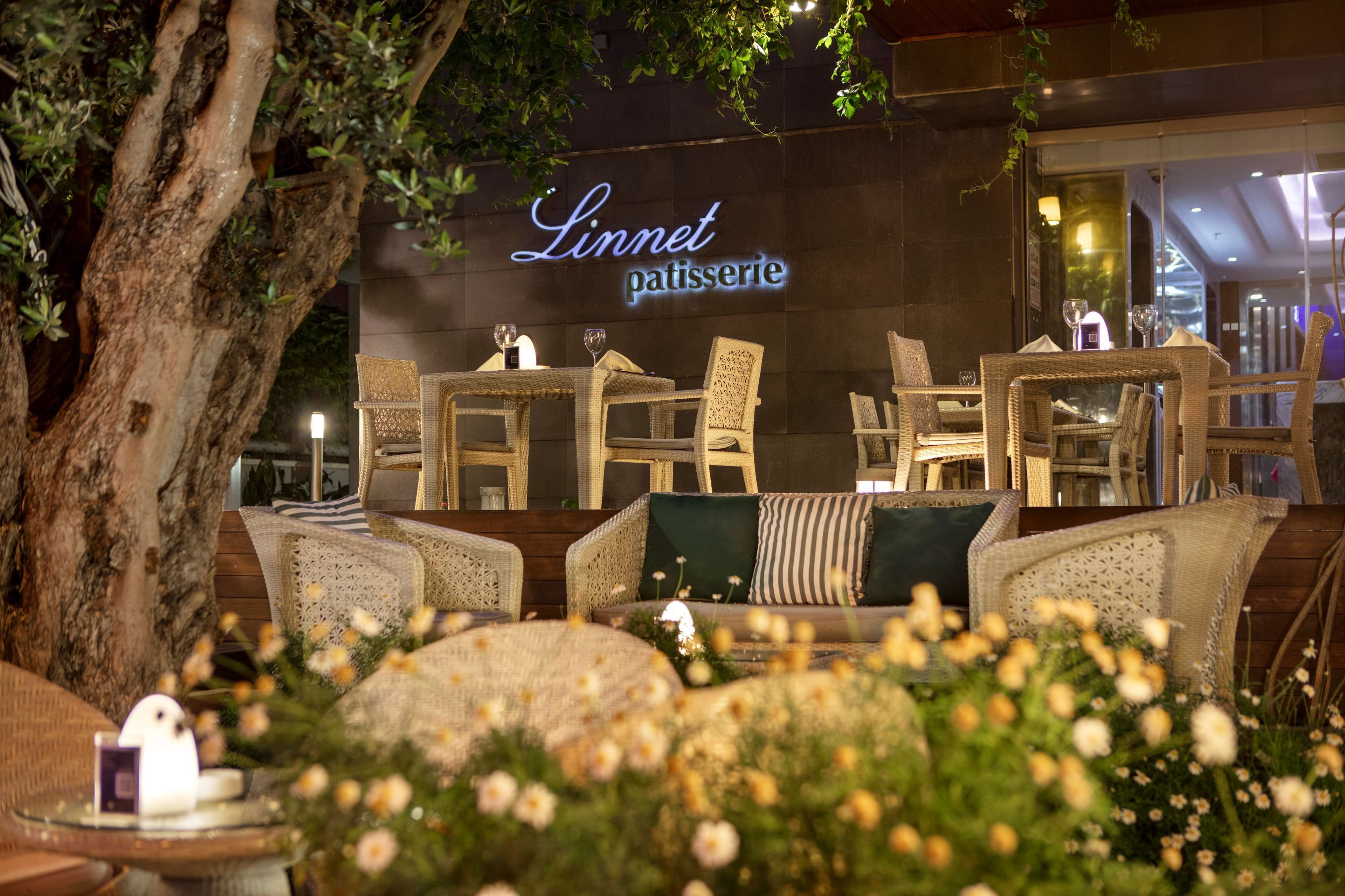 An outdoor seating area with wicker furniture and a sign for 'Linnet patisserie'.
