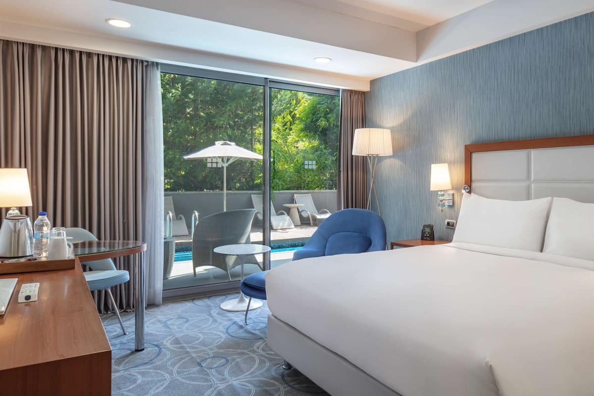 Habitación de hotel con una cama grande, un escritorio con computadora, una silla, una mesita y vista al exterior.