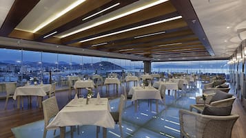 A restaurant with tables and chairs arranged on a glass floor, overlooking a cityscape.