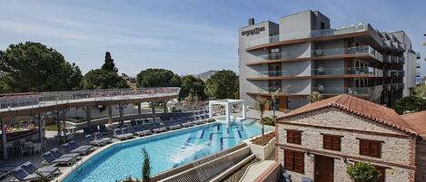 A swimming pool with lounge chairs and a covered area, surrounded by buildings and trees.