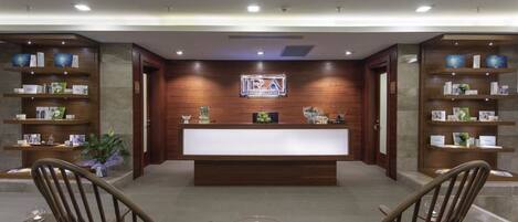 A reception area with a wooden reception desk, shelves with informational brochures, and two chairs with a decorative table in the center.