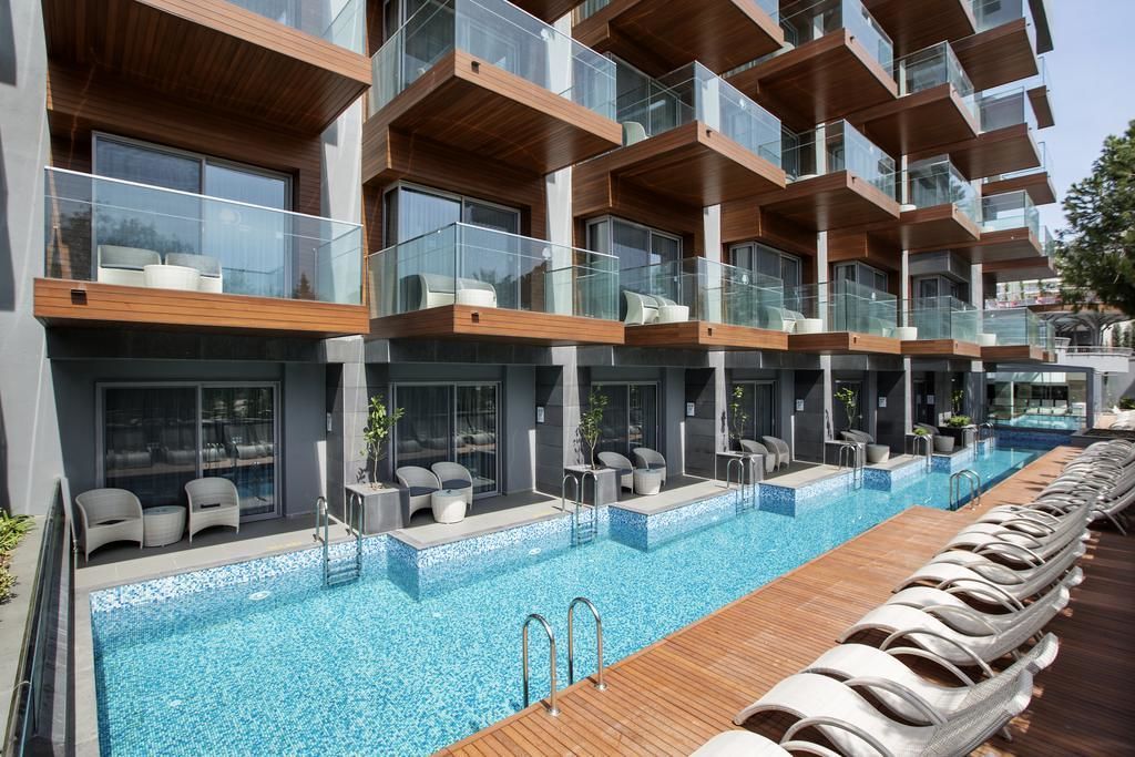 A modern hotel with multiple balconies, a swimming pool, and outdoor seating areas.