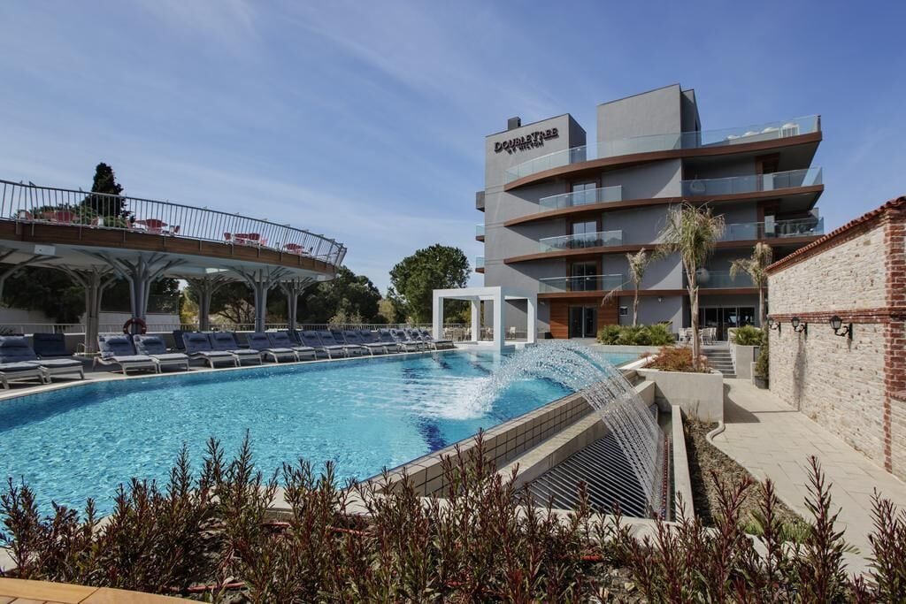 Un hotel moderno con piscina, un paseo cubierto y un edificio de varios pisos con balcones.